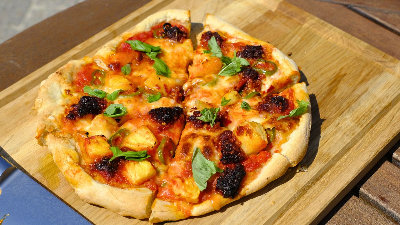 Pizza med nduja og frisk ananas anrettet på skærebræt i egetræ 