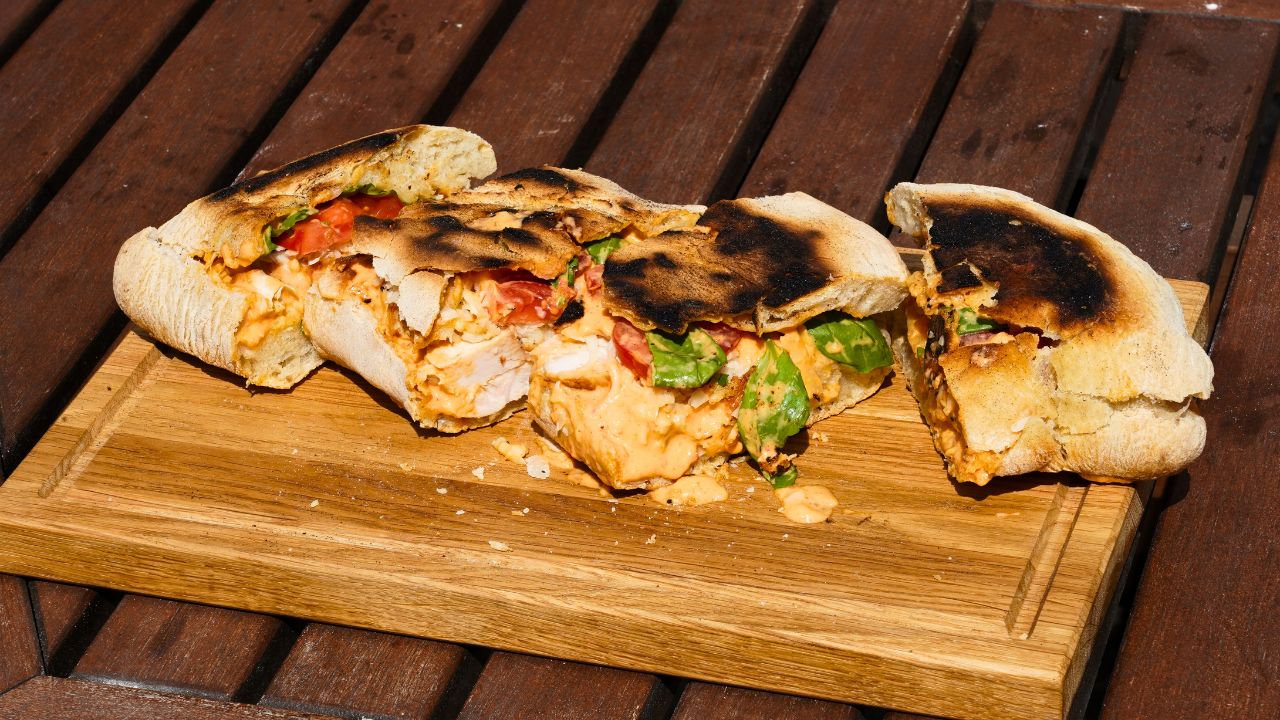 Pizza sandwich med kylling rød pesto og mozzarella anrettet på skærebræt 
