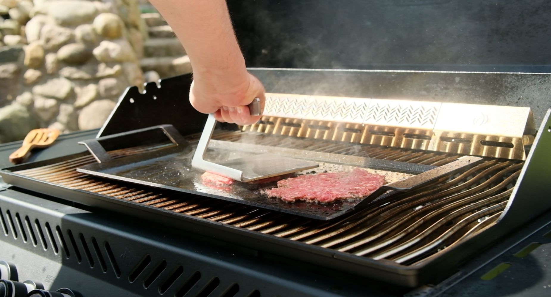 Bøffer presset med smasher i rustfrit stål på stegeplade placeret på gasgrill 