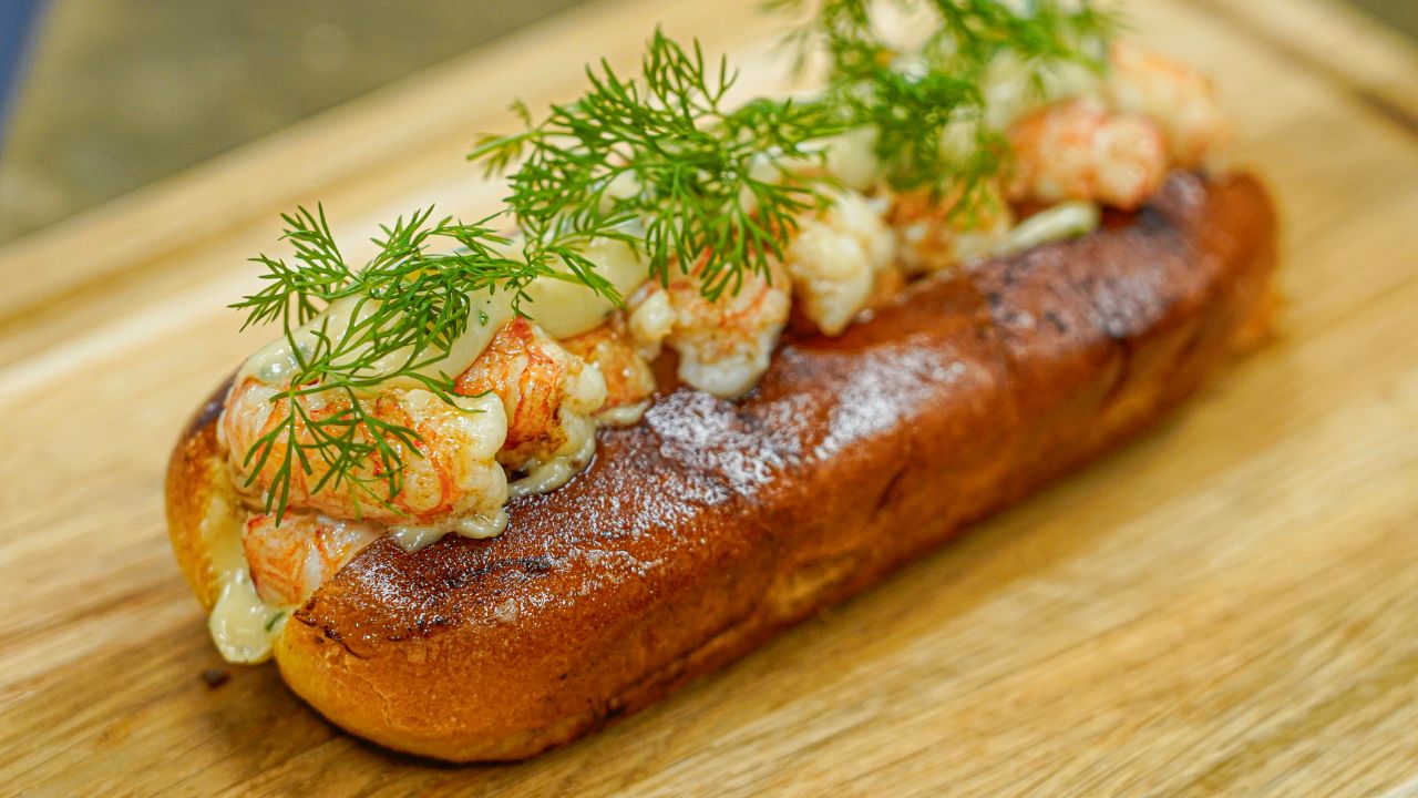 Smørstegt brioche roll med jomfruhummer haler anrettet på skærebræt i egetræ