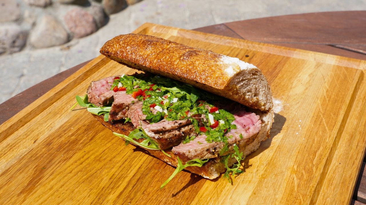 Nærbillede af steaksandwich med chimichurri på grillen anrettet på skærebræt 