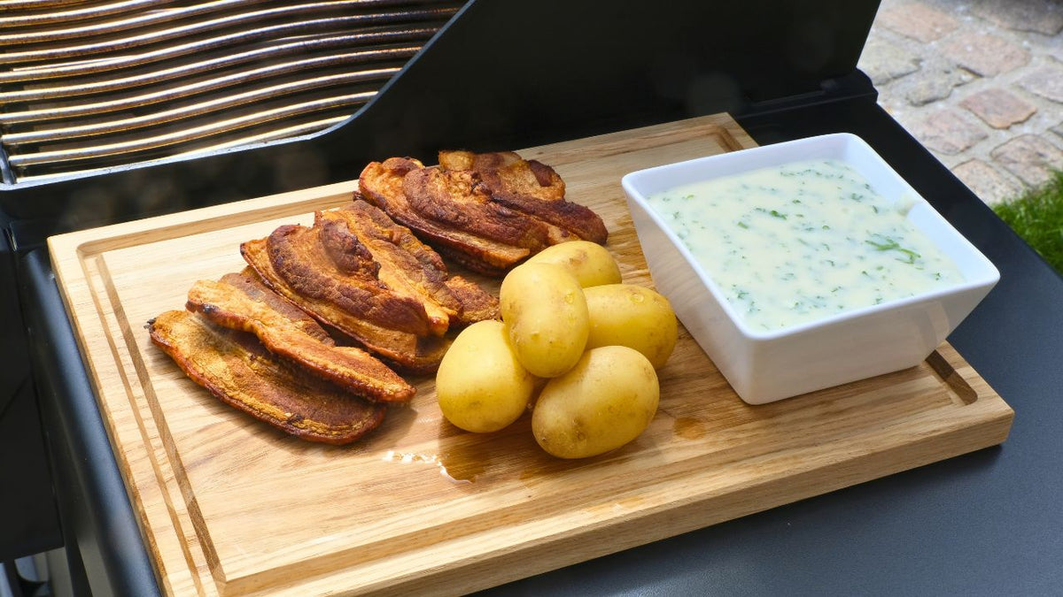 Stegt flæsk med persillesovs anrettet på skærebræt i egetræ ved siden af gasgrill 